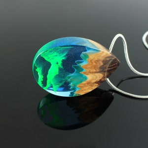 May include: A teardrop-shaped pendant necklace with a silver chain. The pendant is made of clear resin, with a vibrant green and blue design, and a section of natural wood grain. The pendant is approximately 2 inches long.