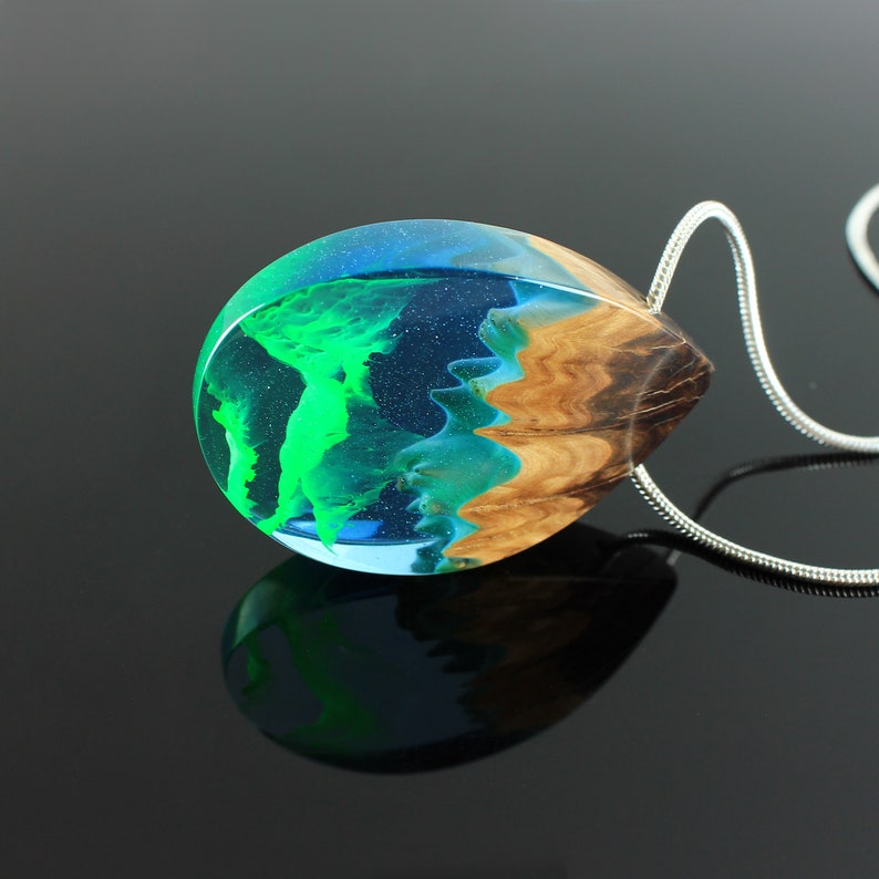 May include: A teardrop-shaped pendant necklace with a silver chain. The pendant is made of clear resin, with a vibrant green and blue design, and a section of natural wood grain. The pendant is approximately 2 inches long.