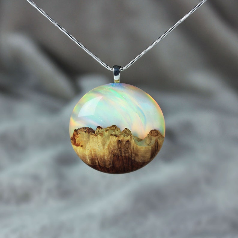 Round pendant handmade with white lab-created opal, wood and resin. Opals iridescent colors shift from blue, green, orange, pink & more, and the wood texture gives the impression of a mountain peaks.