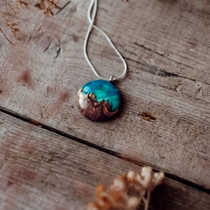 Round pendant handmade with green lab-created opal, burl wood and resin. Opals iridescent colors resemble aurora borealis in motion and the burl wood texture gives the impression of a mountain peaks.