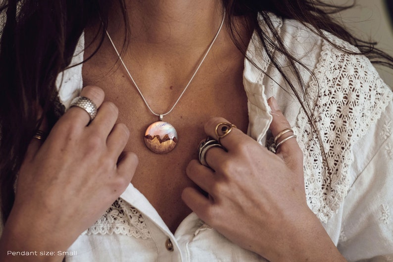 Woman wearing a small sized white Aurora Borealis pendant made of wood, resin, and lab-grown opal with iridescent colors that shift from white, blue, green, orange, pink & more.