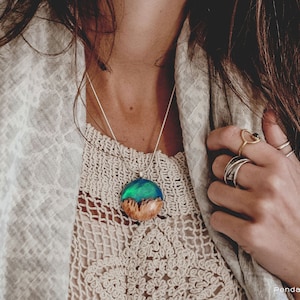 Woman wearing a medium sized green Aurora Borealis pendant made of wood, resin, and lab-grown opal with iridescent colors that shift from blue, green & orange.