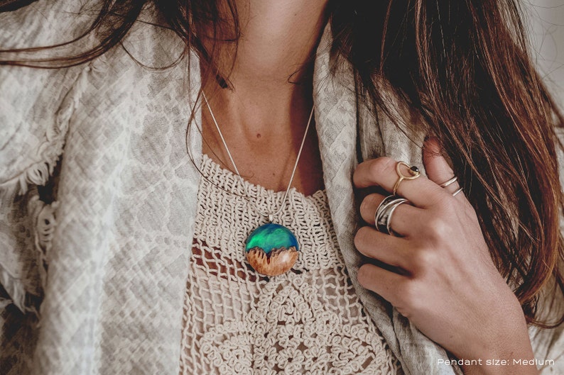 Woman wearing a medium sized green Aurora Borealis pendant made of wood, resin, and lab-grown opal with iridescent colors that shift from blue, green & orange.