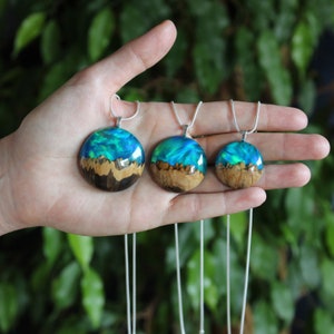 May include: Three silver chain necklaces with round pendants made of wood and blue resin. The pendants feature a swirling blue and green pattern reminiscent of ocean waves.