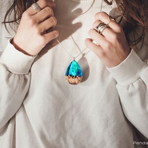Woman wearing a large sized green Aurora Borealis pendant made of wood, resin, and lab-grown opal with iridescent colors that shift from blue, green & orange.