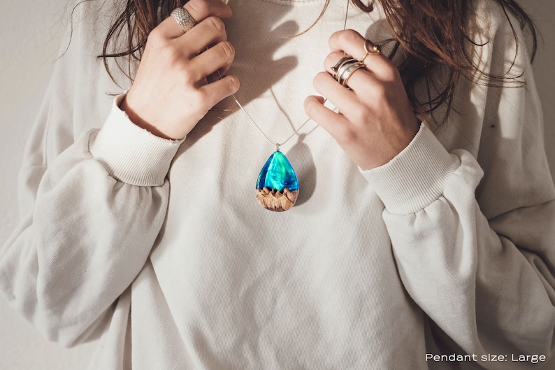 Woman wearing a large sized green Aurora Borealis pendant made of wood, resin, and lab-grown opal with iridescent colors that shift from blue, green & orange.