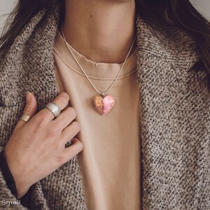 Woman wearing a heart shaped pink Aurora Borealis pendant made of wood, resin, and lab-grown opal with iridescent colors that shift from purple to pink to green, red and more.