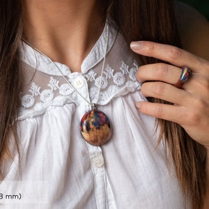 Woman wearing a large sized Aurora Borealis pendant made of wood, resin, and red lab-grown opal with iridescent colors that shift from green, blue, red, orange & more.