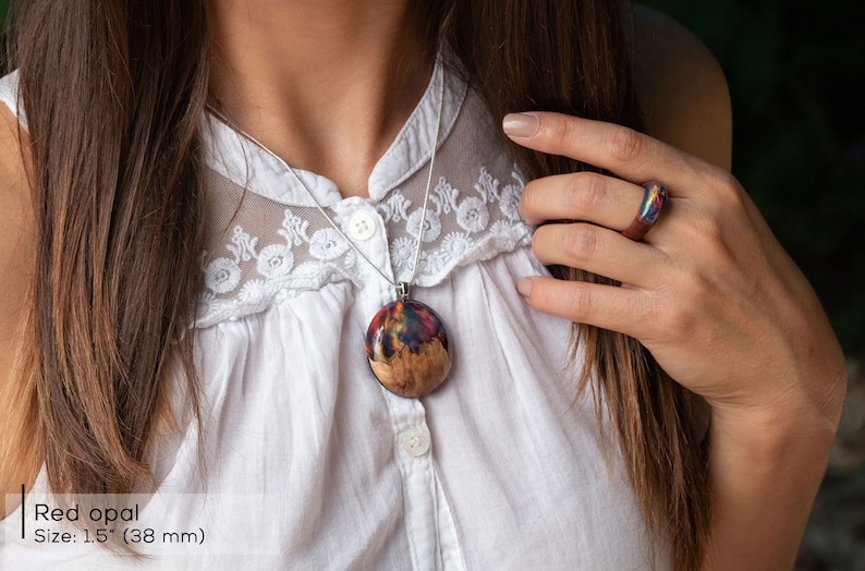 Woman wearing a large sized Aurora Borealis pendant made of wood, resin, and red lab-grown opal with iridescent colors that shift from green, blue, red, orange & more.