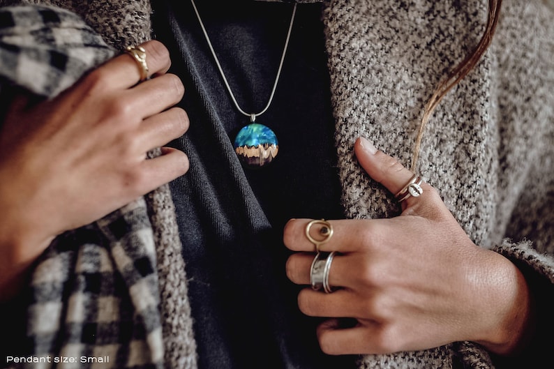 Woman wearing a small sized Aurora Borealis pendant made of wood, resin, and green lab-grown opal with iridescent colors that shift from blue, green & orange.