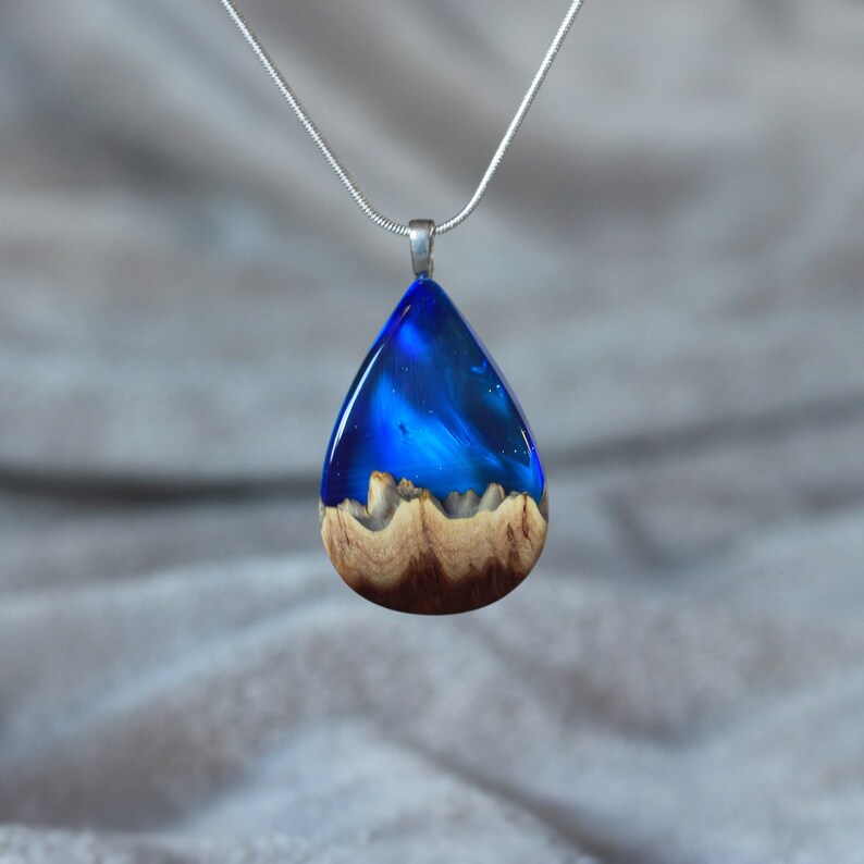 Teardrop pendant handmade with blue lab-created opal, wood and resin. Opals iridescent colors shift from shades of light and dark blue, and the wood texture gives the impression of a mountain peaks.