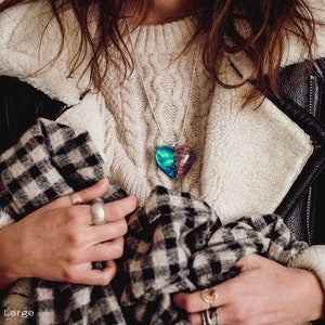 Woman wearing a heart shaped green Aurora Borealis pendant made of wood, resin, and lab-grown opal with iridescent colors that shift from blue, green & orange.