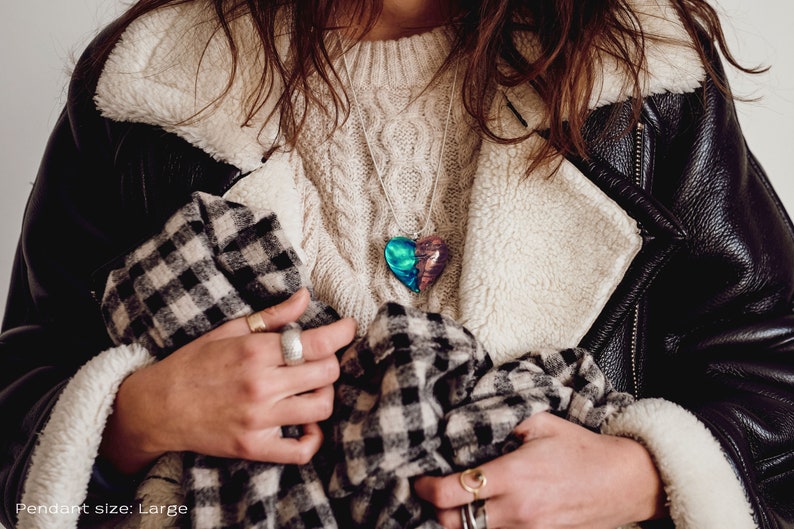 Woman wearing a heart shaped green Aurora Borealis pendant made of wood, resin, and lab-grown opal with iridescent colors that shift from blue, green & orange.
