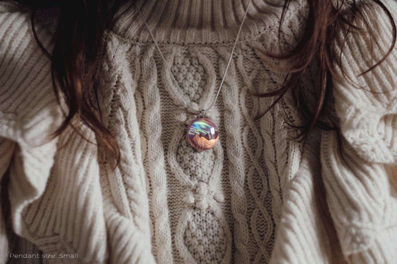 Woman wearing a small sized red Aurora Borealis pendant made of wood, resin, and lab-grown opal with iridescent colors that shift from green, blue, red, orange & more.