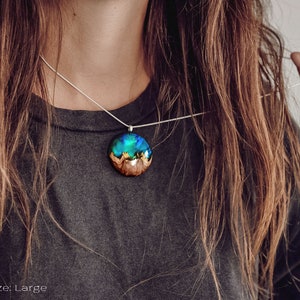 Woman wearing a large sized Aurora Borealis pendant made of wood, resin, and green lab-grown opal with iridescent colors that shift from blue, green & orange.