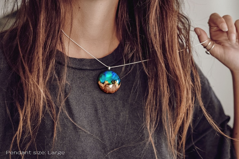 Woman wearing a large sized Aurora Borealis pendant made of wood, resin, and green lab-grown opal with iridescent colors that shift from blue, green & orange.