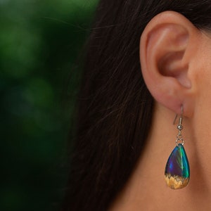 Woman wearing a teardrop green Aurora Borealis pendant made of wood, resin, and purple lab-grown opal with iridescent colors that shift from blue, green & orange.