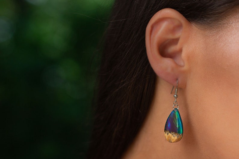 Woman wearing a teardrop green Aurora Borealis pendant made of wood, resin, and purple lab-grown opal with iridescent colors that shift from blue, green & orange.