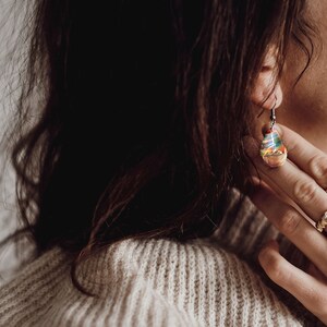 Woman wearing a teardrop red Aurora Borealis earrings made of wood, resin, and purple lab-grown opal with iridescent colors that shift from green, blue, red, orange & more.