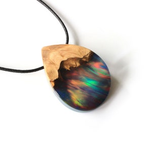 Hand holding Aurora Borealis teardrop pendant made of wood and resin, featuring red lab-grown opal with iridescent colors changing from red, green, blue, orange & more.