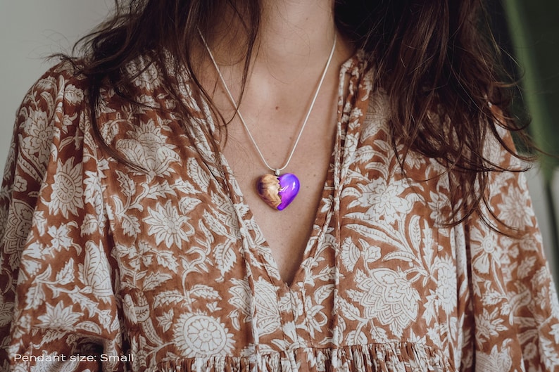 Woman wearing a heart shaped purple Aurora Borealis pendant made of wood, resin, and lab-grown opal with iridescent colors that shift from purple to pink, blue, teal, and more.