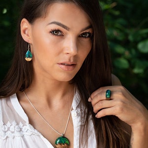 Woman wearing a green Aurora Borealis earrings, pendant and ring made of wood, resin, and purple lab-grown opal with iridescent colors that shift from blue, green & orange.