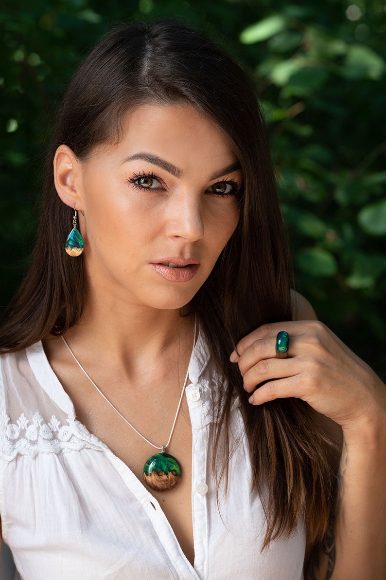 Woman wearing a green Aurora Borealis earrings, pendant and ring made of wood, resin, and purple lab-grown opal with iridescent colors that shift from blue, green & orange.