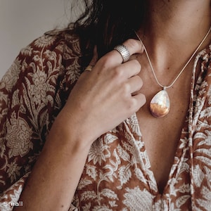 Woman wearing a small sized white Aurora Borealis pendant made of wood, resin, and lab-grown opal with iridescent colors that shift from white, blue, green, orange, pink & more.