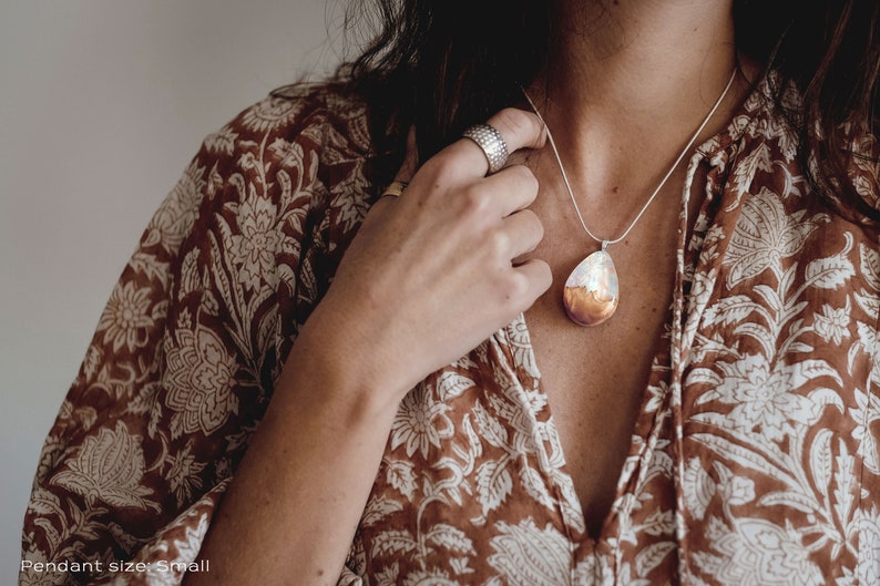 Woman wearing a small sized white Aurora Borealis pendant made of wood, resin, and lab-grown opal with iridescent colors that shift from white, blue, green, orange, pink & more.