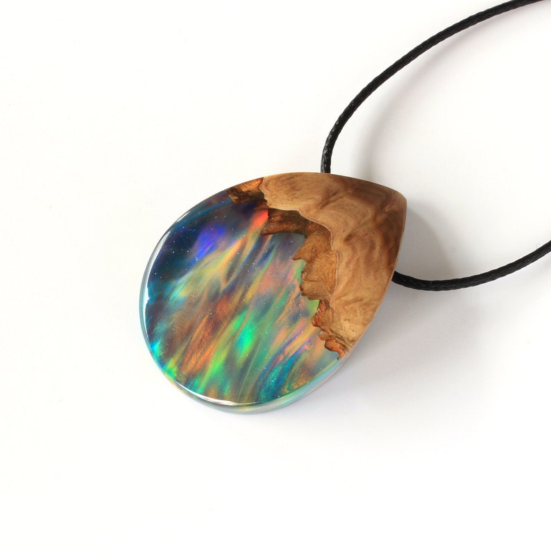 Hand holding Aurora Borealis teardrop pendant made of wood and resin, featuring red lab-grown opal with iridescent colors changing from red, green, blue, orange & more.