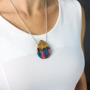 Woman wearing a sized Aurora Borealis pendant made of wood, resin, and red lab-grown opal with iridescent colors that shift from red, green, blue, orange & more.
