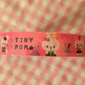 May include: Pink washi tape with a repeating pattern of white cartoon bears wearing overalls and hats. The text "TINY POM" is printed on the tape.