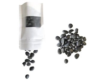 May include: A white resealable pouch with black stones spilling out. The pouch has a clear window showing the black stones inside. A pile of black stones is also shown on a white background.