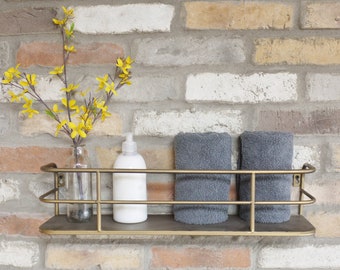 May include: Gold metal wall shelf with two gray towels, a bottle of lotion, and a vase with yellow flowers.