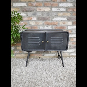 May include: Black metal cabinet with two doors and a distressed finish. The cabinet has four black metal legs and gold-toned handles.