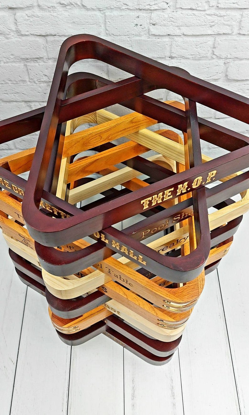 There is a top view of a stack of twelve pool triangles against a white background. There is a various amount of light and dark triangles and brass accented triangles. Each triangle is engraved with a different saying such as The Crocketts Pool Hall