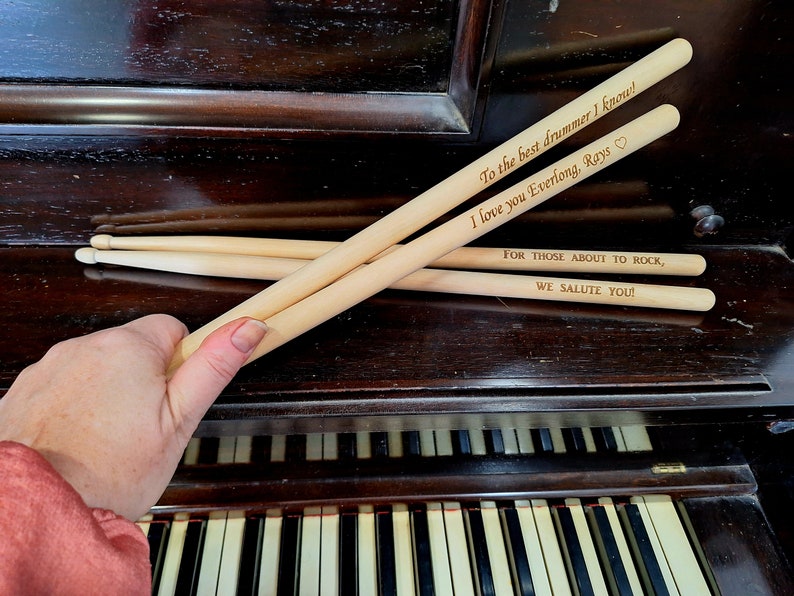 Puede incluir: Tres baquetas de madera con mensajes personalizados. La baqueta superior dice "To the best drummer I know! I love you Everlong, Rays." La baqueta del medio dice "FOR THOSE ABOUT TO ROCK, WE SALUTE YOU!"