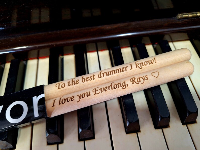 Puede incluir: Dos baquetas de madera con un mensaje personalizado: "To the best drummer I know! I love you Everlong, Rays" con un s&iacute;mbolo de coraz&oacute;n.