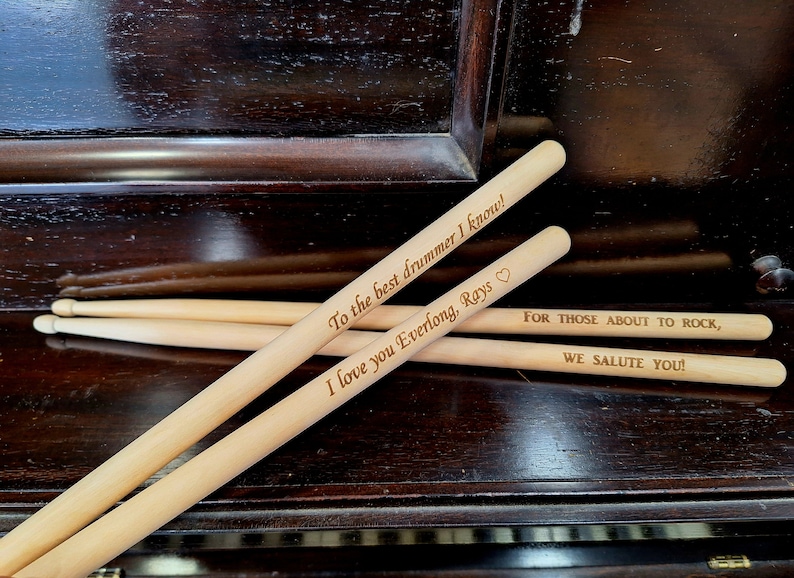 Puede incluir: Tres baquetas de madera con mensajes personalizados. La baqueta superior dice "To the best drummer I know! I love you Everlong, Rays." La baqueta inferior dice "FOR THOSE ABOUT TO ROCK, WE SALUTE YOU!"