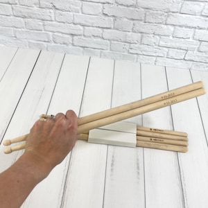 Puede incluir: Un juego de baquetas de madera con grabados personalizados. La baqueta superior tiene la fecha "9-16-2015" grabada dos veces. La baqueta inferior tiene el texto "Te amo" y "Feliz D&iacute;a de San Valent&iacute;n" grabado.