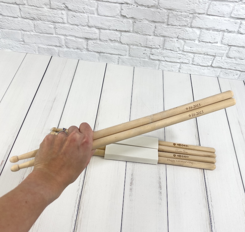 Puede incluir: Un juego de baquetas de madera con grabados personalizados. La baqueta superior tiene la fecha "9-16-2015" grabada dos veces. La baqueta inferior tiene el texto "Te amo" y "Feliz D&iacute;a de San Valent&iacute;n" grabado.