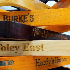 There is a close up view of a stack of twelve pool triangles against a white background. There is a various amount of light and dark triangles and brass accented triangles. Each triangle is engraved with a different sayings.