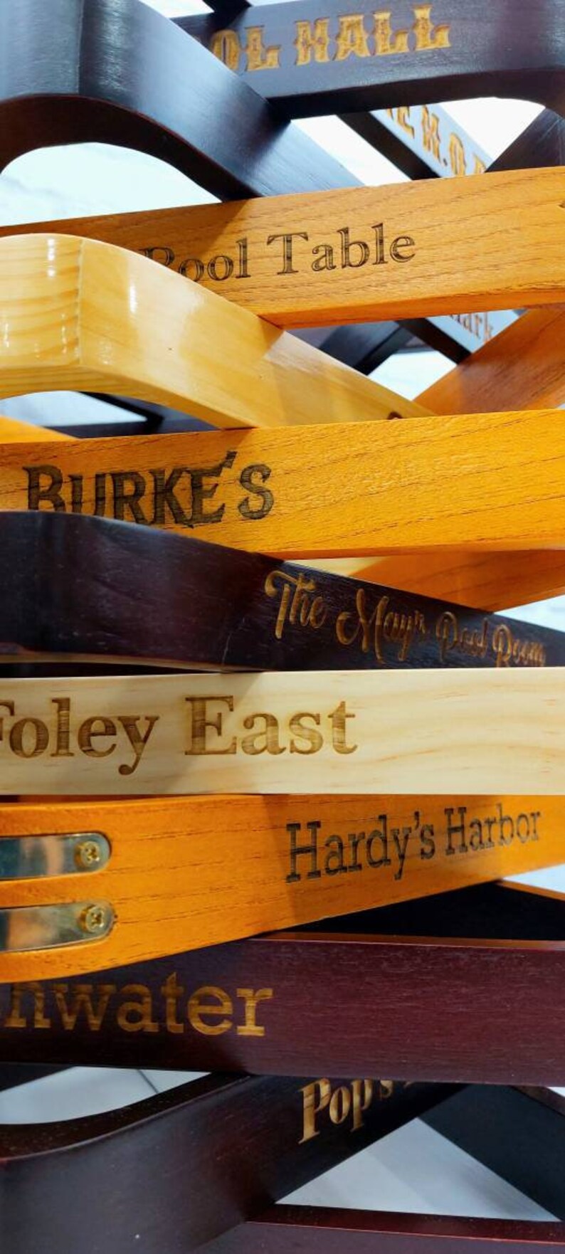 There is a close up view of a stack of twelve pool triangles against a white background. There is a various amount of light and dark triangles and brass accented triangles. Each triangle is engraved with a different sayings.