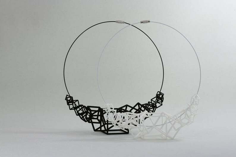Puede incluir: Dos collares, uno negro y otro blanco, hechos de formas geom&eacute;tricas. Los collares est&aacute;n hechos de alambre fino y est&aacute;n conectados por un cierre.
