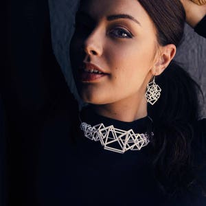 Puede incluir: Una mujer con un top negro, un collar blanco geom&eacute;trico y pendientes a juego. El collar y los pendientes est&aacute;n hechos de material impreso en 3D.