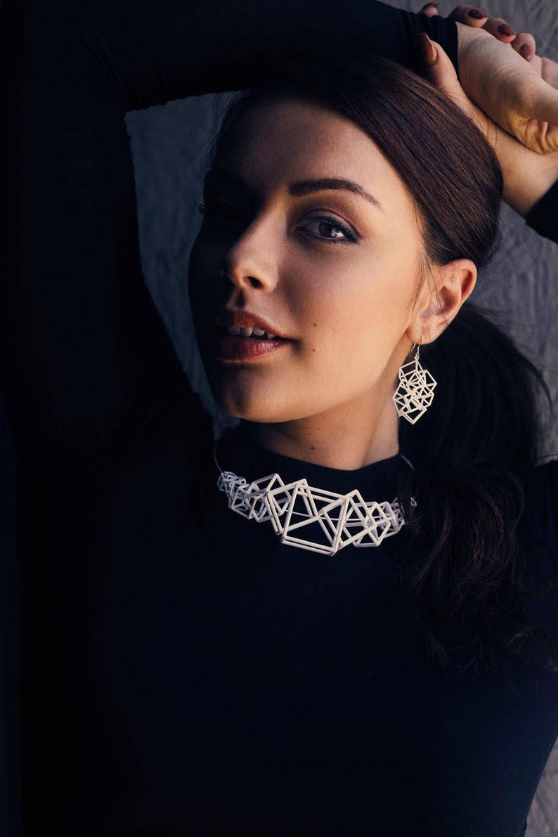 Puede incluir: Una mujer con un top negro, un collar blanco geom&eacute;trico y pendientes a juego. El collar y los pendientes est&aacute;n hechos de material impreso en 3D.