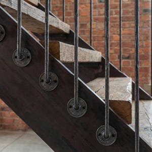 May include: Close-up of a staircase with dark wood steps and metal railings. The steps are made of reclaimed wood, and the metal railings are attached with circular plates that read "Made in England". The background is a brick wall.