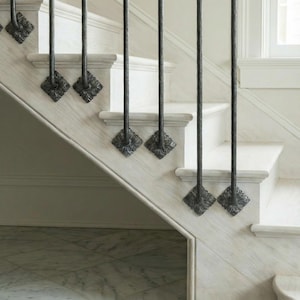 May include: A close-up of a staircase with white wooden steps and decorative black metal balusters. The balusters have a floral design at the base and are evenly spaced along the stairs.