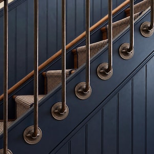 Può includere: Una scala con pareti a pannelli verticali blu scuro e gradini coperti da un tappeto con motivo pied-de-poule marrone e crema. I corrimano verticali in bronzo sono fissati al lato della scala con supporti a parete circolari in bronzo.