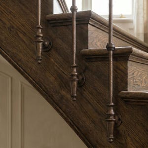 May include: Close-up of a wooden staircase with decorative metal balusters. The balusters are a dark bronze colour and are attached to the wooden steps with circular mounts. The wood has a rich, dark brown finish. The staircase is near a window.